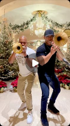 two men playing trombones in front of christmas trees