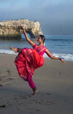 a woman is dancing on the beach by the water