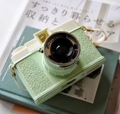 an old camera sitting on top of a green book next to a pair of scissors