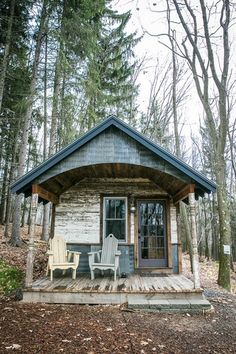 two chairs are sitting on the front porch of a small cabin in the woods,