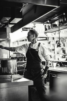 a man standing in a kitchen next to a pot and pan on a stove top