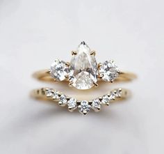 an engagement and wedding ring set with a pear shaped diamond in the center, on a white background