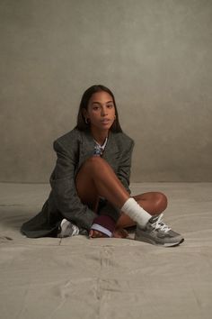 a woman sitting on top of a bed in a suit and socks with her legs crossed