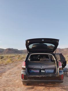 the back end of a car with its trunk open on a dirt road in the desert