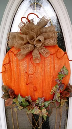 an orange pumpkin decorated with burlocks and twine bows on the front door