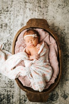 a newborn baby wrapped in a pink blanket is laying on a wooden bowl with its head resting on the pillow