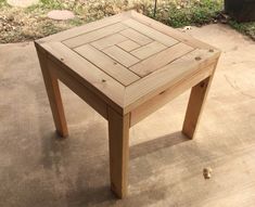 a small wooden table sitting on top of a cement floor next to a trash can