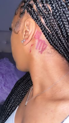 a woman with cornrows has pink ink on her face and behind her ear