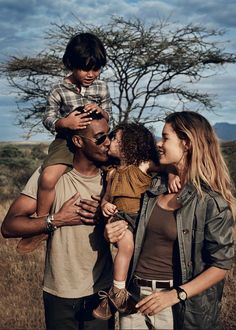 a man, woman and child are standing in front of a tree with their hands around each other