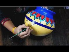 a woman is painting a vase on the floor with paintbrushes and a pen