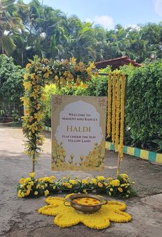 a welcome sign with yellow flowers around it and a bowl of food on the ground