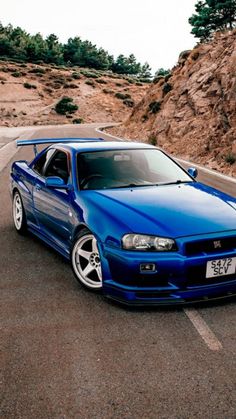 a blue sports car parked in a parking lot next to some rocks and trees on the side of the road