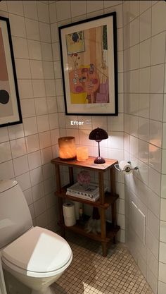 a white toilet sitting next to a wooden shelf in a bathroom under a painting on the wall