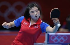 a woman holding a ping pong racquet on top of a tennis court