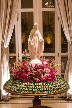 the statue is surrounded by flowers in front of a window