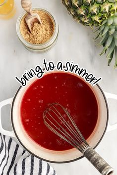 a bowl filled with red liquid next to pineapples and other ingredients on a table