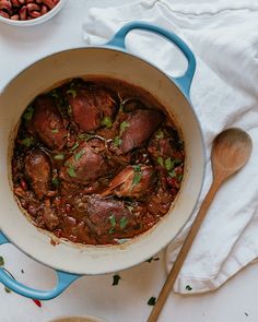 a pot filled with meat and vegetables on top of a white cloth next to a wooden spoon