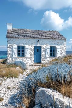 an old stone house sitting on top of a rocky beach next to the ocean with blue doors