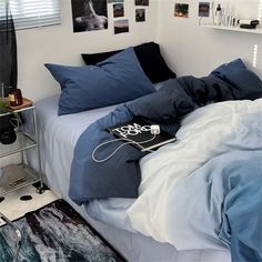 an unmade bed with blue sheets and black pillows in a white room next to pictures on the wall