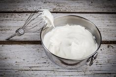 a metal bucket filled with white cream next to a whisk on top of a wooden table