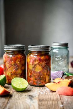 two mason jars filled with pickled fruit and vegetables next to sliced apples on a wooden table