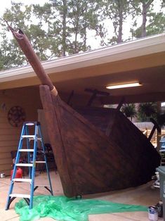 a large wooden boat sitting on top of a garage floor next to a ladder and other tools