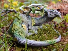 a statue of a lizard sitting on top of green moss in the grass next to flowers