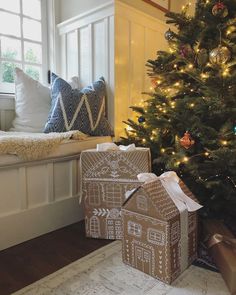 a christmas tree with presents under it in front of a window and a small gingerbread house on the floor