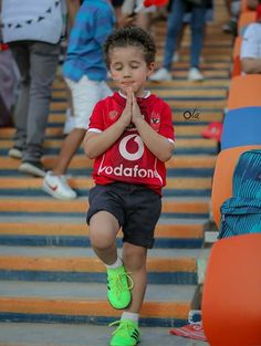 a young boy in red shirt and black shorts standing on steps with his hands together