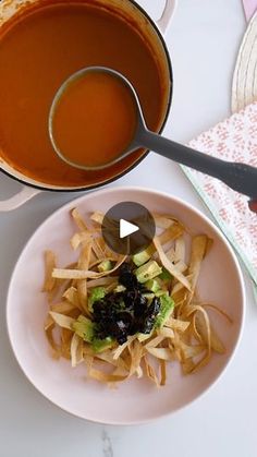 a white plate topped with pasta next to a pot of tomato soup and a spoon