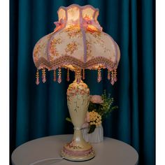 a lamp that is on top of a table with flowers in the vase next to it