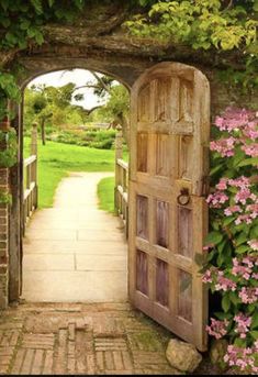 an open wooden door leading into a lush green garden with pink flowers on either side