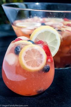 two glasses filled with fruit and ice sitting on top of a black table next to each other