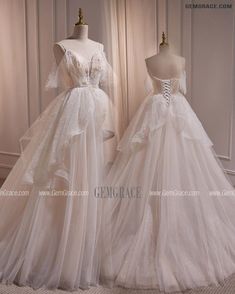 two wedding gowns on mannequins in front of a white wall with curtains