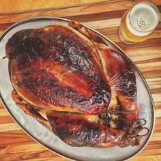 a roasted turkey on a platter next to a glass of beer