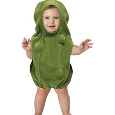 a baby in a green frog costume standing on one leg and smiling at the camera