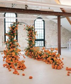 an arrangement of orange flowers sitting on the floor in front of two large windows with exposed beams