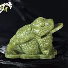 a green frog figurine sitting on top of a black surface next to a white flower