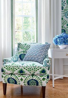 a green and white chair sitting in front of a window next to a table with flowers on it