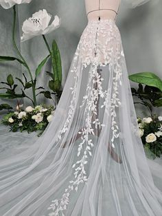 a wedding veil with white flowers and leaves on the bottom is hanging from a mannequin