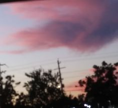 the sky is pink and blue with some clouds in front of trees at night time