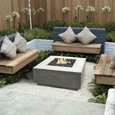 an outdoor fire pit surrounded by wooden benches and pillows on top of each other in the middle of a garden