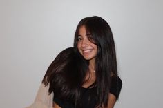 a smiling woman with long dark hair and black shirt, standing in front of a white wall