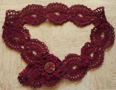 a red crocheted scarf with flowers on it sitting on a table next to a wooden floor