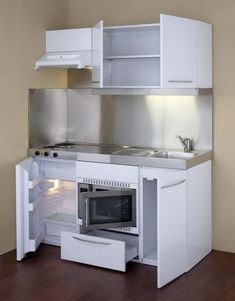 a small kitchen with white cabinets and an open microwave oven in the center, on top of a hard wood floor