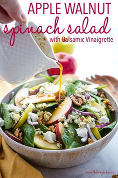 a person pouring dressing into a salad in a bowl with apples and spinach on the side