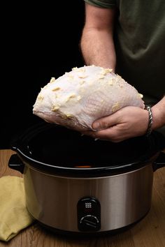 a man holding a piece of chicken over an electric crock pot on a wooden table