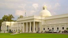 a large white building with columns and a clock tower on it's side in the middle of a grassy area