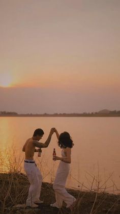 two people are dancing by the water at sunset