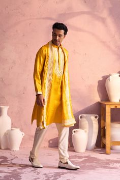 Shrestha by Vastramay - Men's Yellow Silk Kurta Pyjama Set Luxuriate in this elegant yellow silk kurta pyjama set featuring intricate machine embroidery. Perfect for festive occasions or special events. Key Features Yellow silk kurta with machine embroidery on neckline Mandarin collar, long sleeves, side slits, and pockets Cream colored pyjama with elasticated waistband Yellow embroidered silk dupatta Specifications Kurta Length: Knee Length Material & Care Top Fabric: Silk Blend Bottom: Cream colored pyjama fabric (material not specified on source website) Dupatta: Silk Dry Clean Only Legal Disclaimer: The product is guaranteed to be 100% genuine. Product images are for illustrative purposes only. Images/packaging/ labels may vary from time to time due to changes made by the manufacturer' Yellow Salwar Kameez With Straight Kurta, Yellow Straight Kurta Salwar Kameez For Seasonal Wear, Festive Mustard Kurta With Resham Embroidery, Traditional Yellow Chanderi Sherwani, Yellow Straight Kurta For Navratri, Yellow Chanderi Sherwani With Traditional Drape, Yellow Sherwani With Resham Embroidery In Chanderi, Designer Yellow Chanderi Sherwani, Yellow Chanderi Sherwani With Resham Embroidery